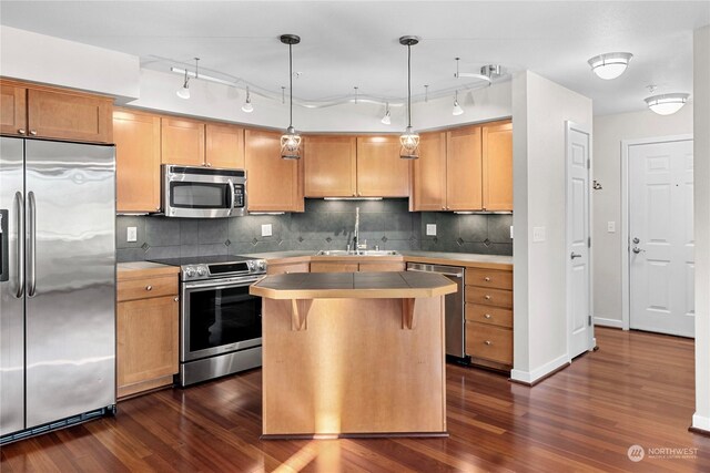 kitchen featuring sink, appliances with stainless steel finishes, hanging light fixtures, backsplash, and a kitchen island