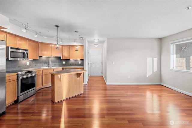 kitchen featuring appliances with stainless steel finishes, hanging light fixtures, a center island, tasteful backsplash, and dark hardwood / wood-style flooring