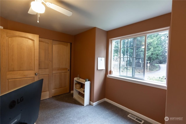 unfurnished office featuring ceiling fan and dark colored carpet