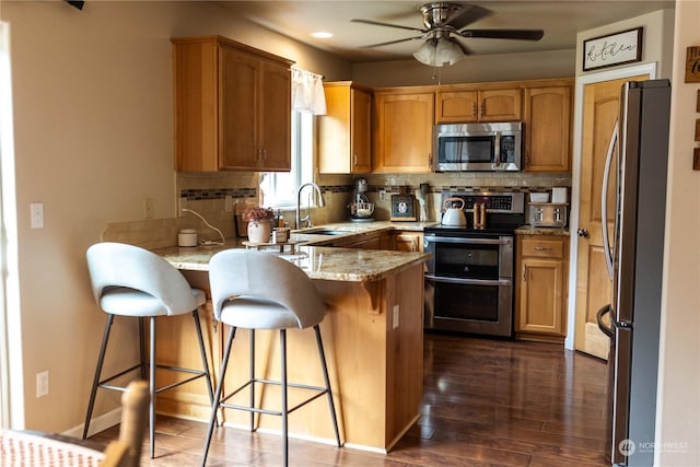 kitchen with sink, appliances with stainless steel finishes, a kitchen breakfast bar, kitchen peninsula, and backsplash