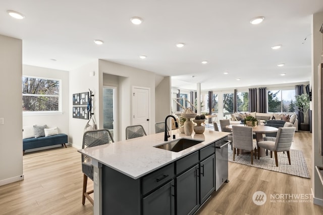 kitchen with sink, a breakfast bar area, dishwasher, light stone countertops, and a center island with sink