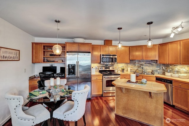 kitchen with sink, appliances with stainless steel finishes, hanging light fixtures, backsplash, and dark hardwood / wood-style flooring