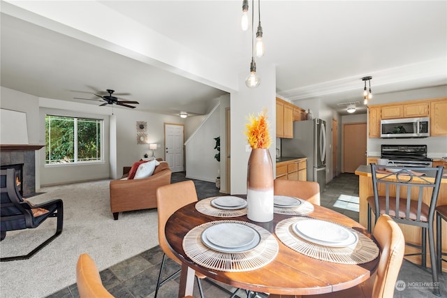 carpeted dining area with a tiled fireplace and ceiling fan