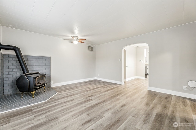 unfurnished living room with ceiling fan, light hardwood / wood-style floors, and a wood stove