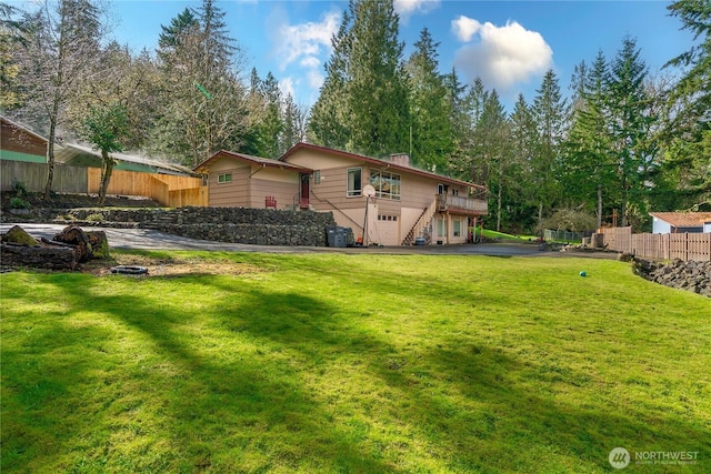 view of yard with an attached garage, a wooden deck, driveway, and fence