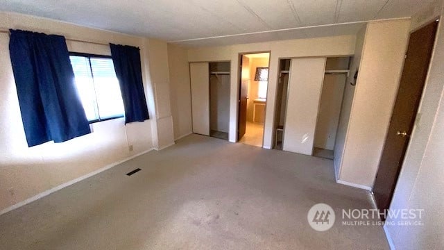 unfurnished bedroom with two closets, carpet floors, and ensuite bathroom