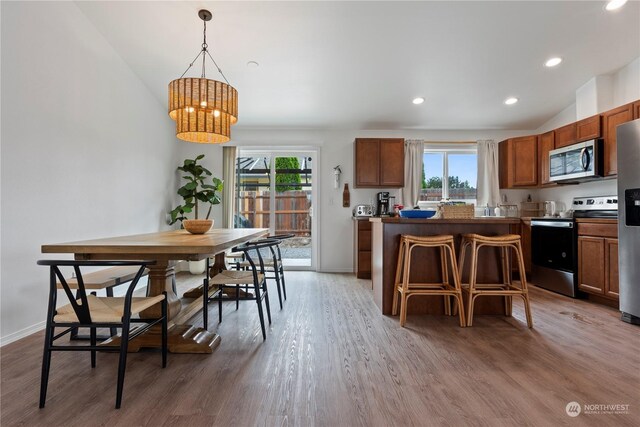 kitchen featuring pendant lighting, lofted ceiling, hardwood / wood-style flooring, appliances with stainless steel finishes, and a kitchen breakfast bar