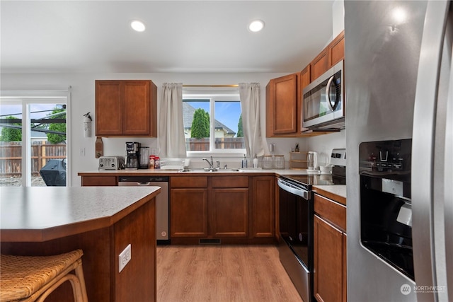 kitchen with appliances with stainless steel finishes, sink, a breakfast bar area, a healthy amount of sunlight, and light hardwood / wood-style flooring