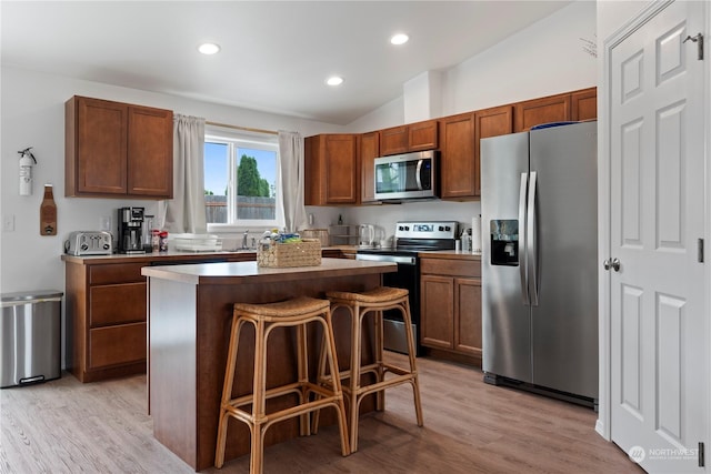 kitchen with lofted ceiling, a kitchen bar, light hardwood / wood-style flooring, appliances with stainless steel finishes, and a kitchen island