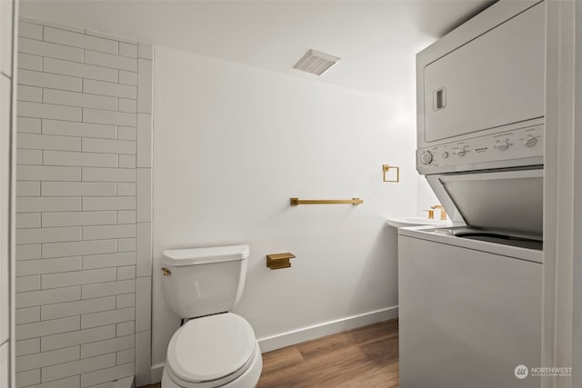 bathroom with stacked washer / drying machine, hardwood / wood-style flooring, and toilet