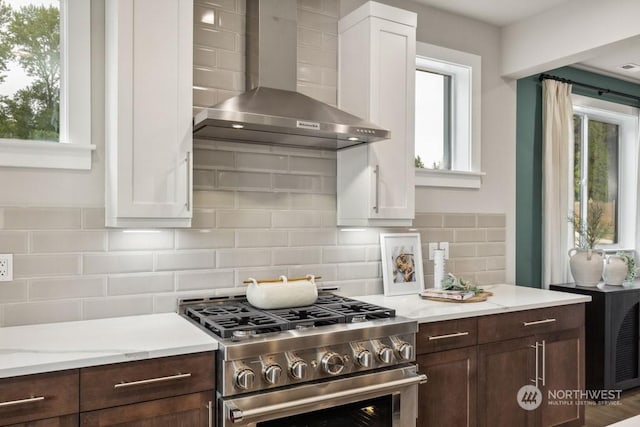 kitchen featuring white cabinetry, backsplash, dark brown cabinets, gas stove, and wall chimney exhaust hood