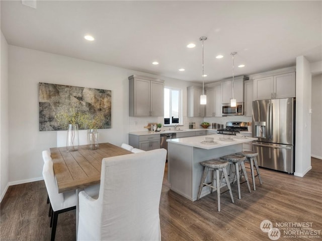 kitchen featuring appliances with stainless steel finishes, dark hardwood / wood-style floors, decorative light fixtures, gray cabinetry, and a center island