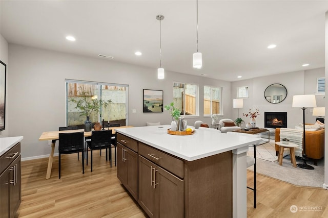 kitchen with pendant lighting, a kitchen breakfast bar, a center island, dark brown cabinets, and light hardwood / wood-style flooring