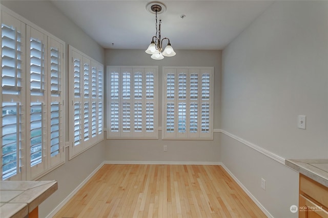 unfurnished dining area with plenty of natural light, light hardwood / wood-style floors, and a notable chandelier