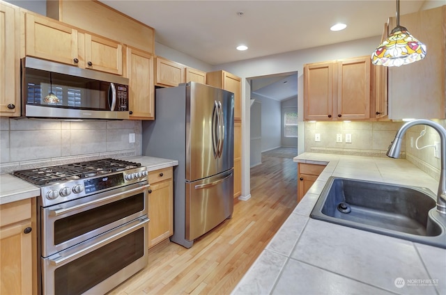 kitchen with stainless steel appliances, sink, tile countertops, and light brown cabinetry