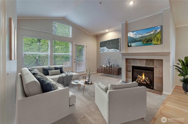 living room with ornamental molding, lofted ceiling, a tiled fireplace, and light hardwood / wood-style floors