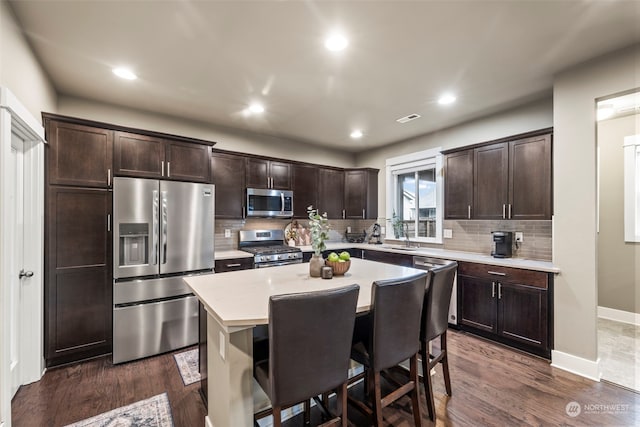 kitchen featuring a breakfast bar, dark brown cabinets, appliances with stainless steel finishes, dark hardwood / wood-style flooring, and a kitchen island