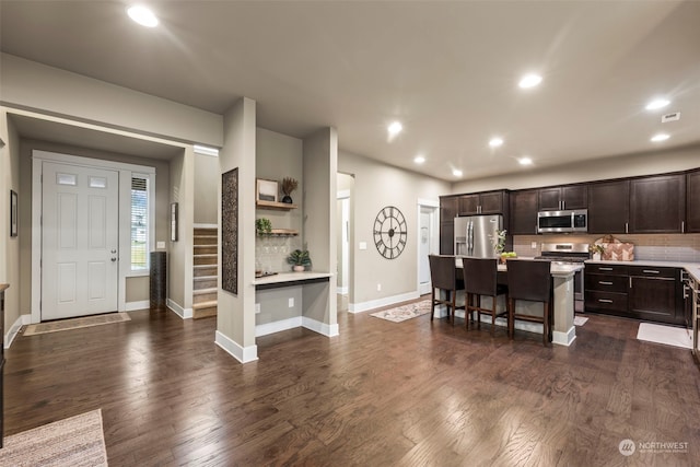 kitchen with a breakfast bar area, dark brown cabinets, dark hardwood / wood-style floors, stainless steel appliances, and a kitchen island with sink