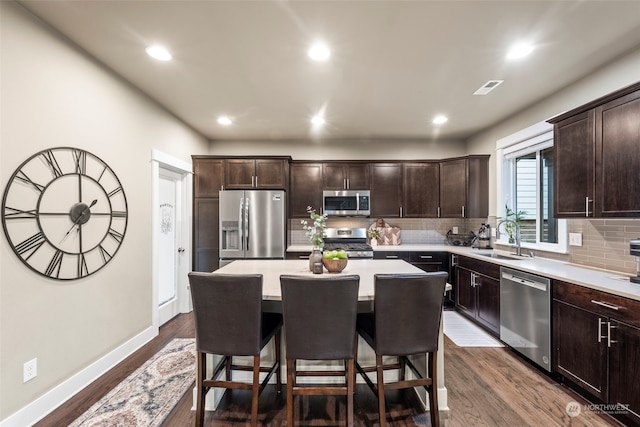 kitchen with sink, backsplash, stainless steel appliances, a center island, and a kitchen bar