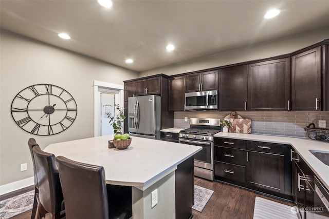 kitchen featuring tasteful backsplash, dark brown cabinets, appliances with stainless steel finishes, dark hardwood / wood-style flooring, and a kitchen island