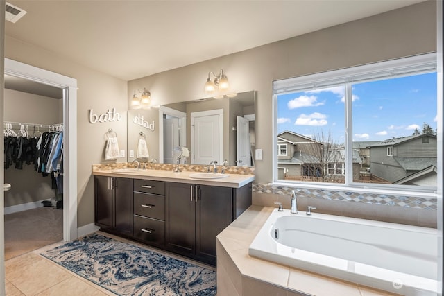 bathroom featuring tile patterned flooring, vanity, and a relaxing tiled tub