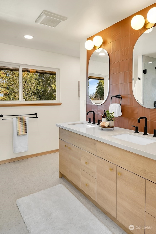 bathroom with double vanity, a sink, visible vents, and baseboards