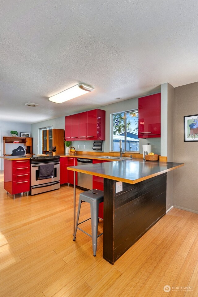 kitchen with sink, light hardwood / wood-style floors, kitchen peninsula, and appliances with stainless steel finishes