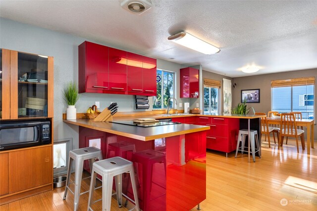 kitchen with sink, a breakfast bar area, a healthy amount of sunlight, kitchen peninsula, and light wood-type flooring