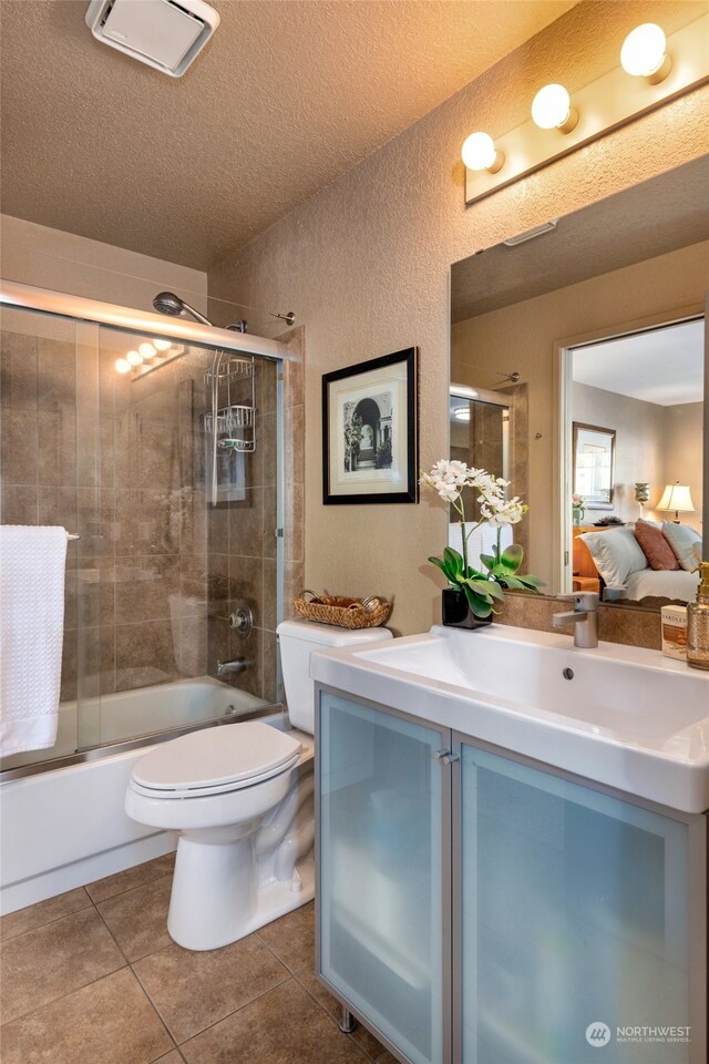 full bathroom with tile patterned floors, toilet, bath / shower combo with glass door, a textured ceiling, and vanity