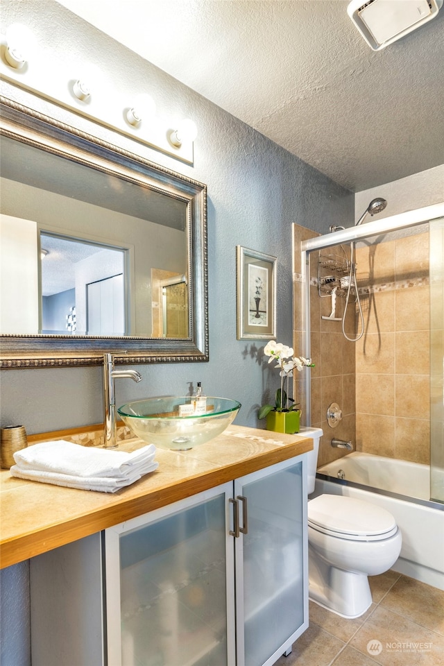 full bathroom with combined bath / shower with glass door, vanity, toilet, tile patterned floors, and a textured ceiling