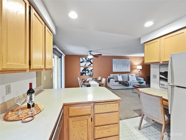 kitchen with white fridge, light brown cabinets, ceiling fan, and kitchen peninsula