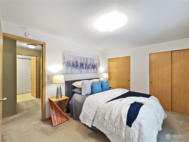 bedroom featuring light colored carpet and multiple closets