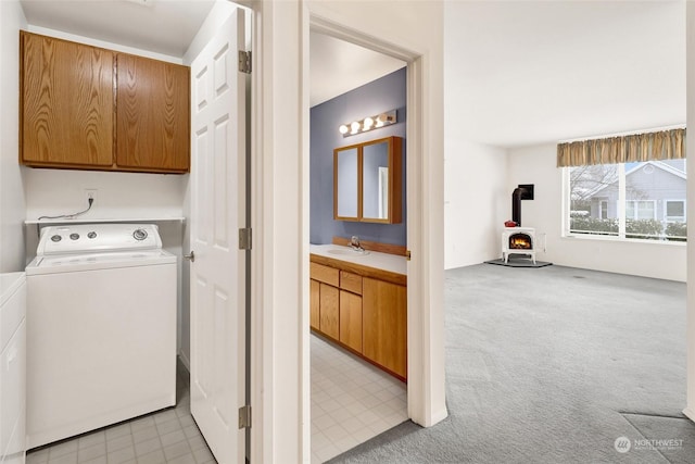 clothes washing area featuring a wood stove, cabinet space, a sink, light carpet, and independent washer and dryer