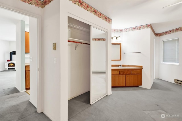 interior space with sink, light colored carpet, a closet, and a wood stove