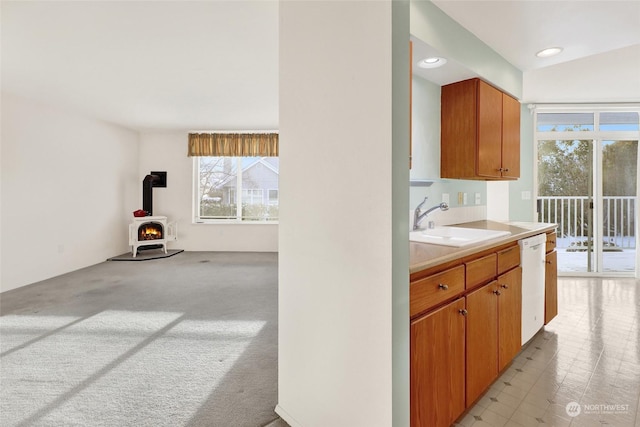 kitchen with a sink, light countertops, light colored carpet, dishwasher, and a wood stove