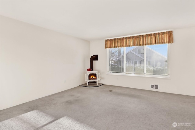 unfurnished room featuring carpet flooring and a wood stove