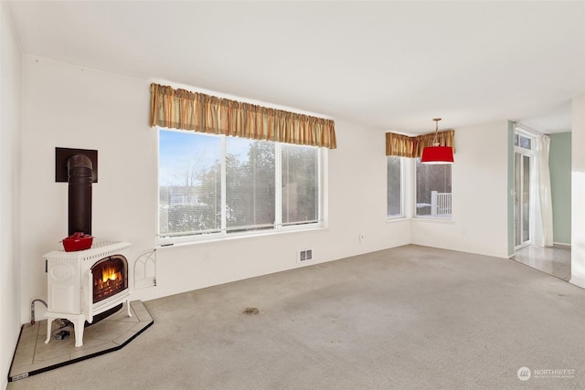 unfurnished living room featuring visible vents, carpet floors, and a wood stove