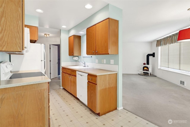 kitchen with sink, white appliances, light colored carpet, and a wood stove