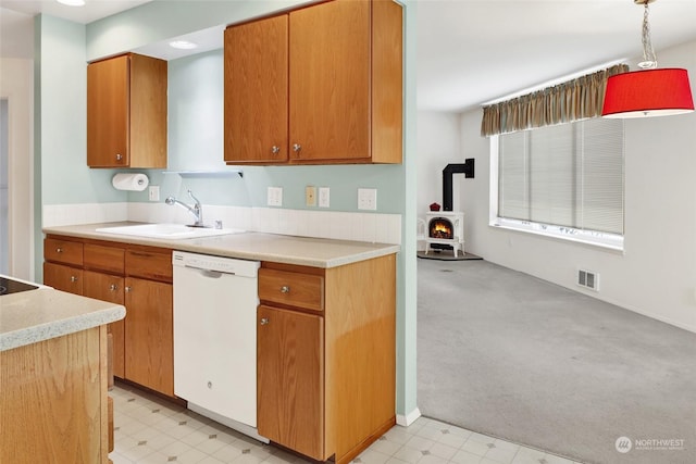 kitchen with sink, a wood stove, light colored carpet, and white dishwasher