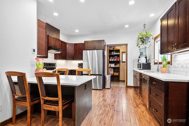 kitchen featuring sink, stainless steel fridge, a breakfast bar area, range, and light wood-type flooring