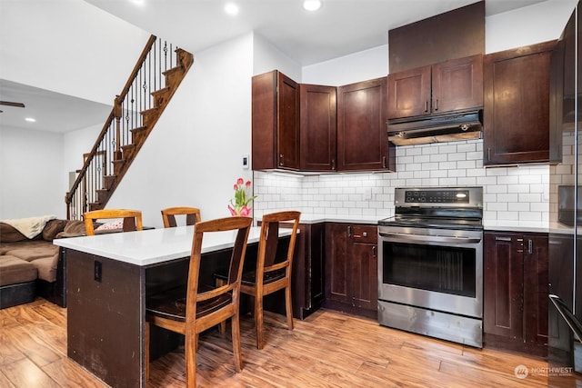 kitchen featuring a breakfast bar area, stainless steel range with electric stovetop, kitchen peninsula, light hardwood / wood-style floors, and decorative backsplash