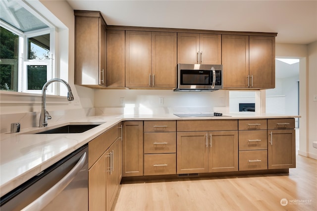 kitchen with light stone counters, sink, light hardwood / wood-style flooring, and appliances with stainless steel finishes