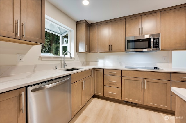 kitchen with light stone counters, sink, stainless steel appliances, and light wood-type flooring