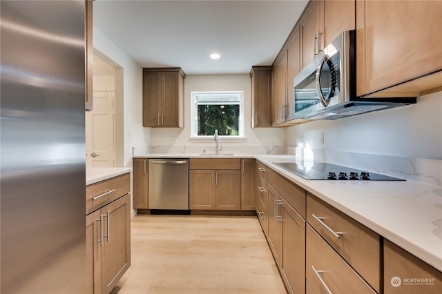 kitchen featuring light stone counters, appliances with stainless steel finishes, sink, and light hardwood / wood-style flooring