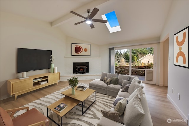 living room with lofted ceiling with skylight, a wood stove, ceiling fan, and light wood-type flooring