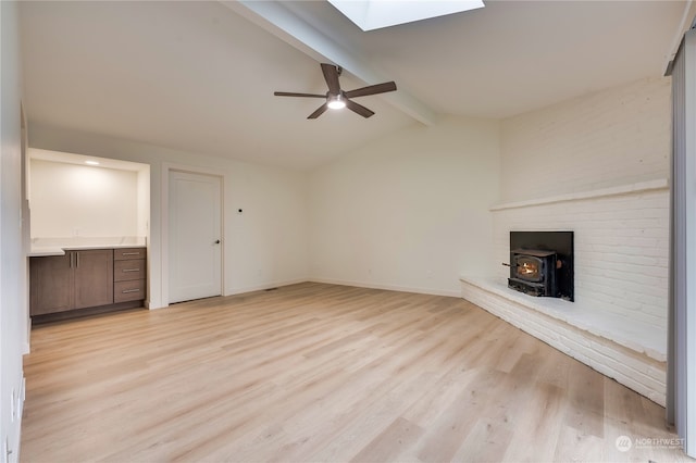 unfurnished living room with ceiling fan, vaulted ceiling with skylight, light hardwood / wood-style floors, and a wood stove