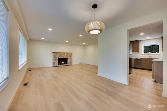 unfurnished living room with a fireplace, sink, and light wood-type flooring