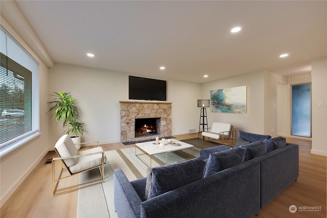 living room with a stone fireplace and light wood-type flooring