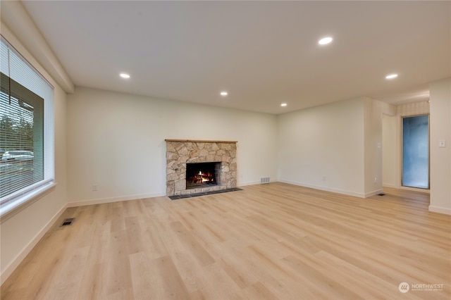 unfurnished living room with a stone fireplace and light hardwood / wood-style floors