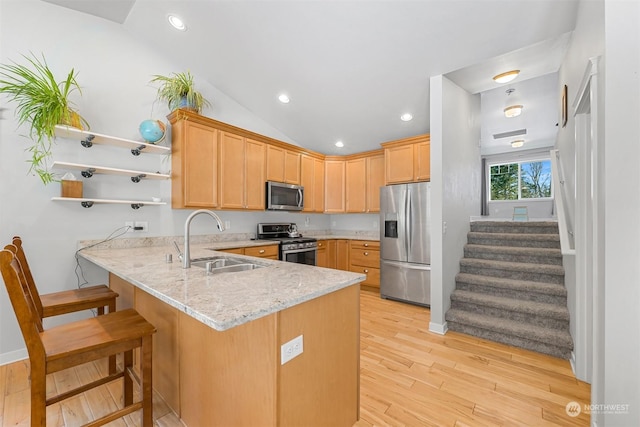 kitchen with sink, stainless steel appliances, light stone counters, light brown cabinetry, and kitchen peninsula